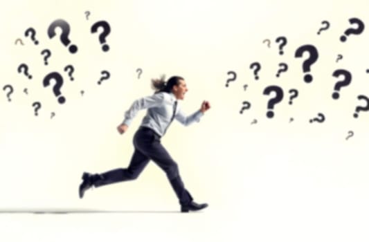 A business professional runs rapidly amid question marks, representing the pressures and uncertainties faced in addressing various challenges. Blurred picture.