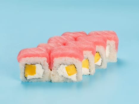 Studio photography of Philadelphia Roll of velvety cream cheese and mango wrapped in perfect seasoned sushi rice and fresh tuna. Isolated on solid light blue background