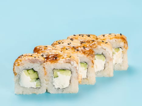Studio photography of Philadelphia Roll of velvety cream cheese and cucumber wrapped in perfect seasoned sushi rice and fresh smoked eel decorated black sesame seeds. Isolated on light blue background