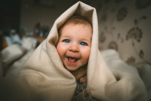 Smiling baby girl crawling on bed under the blanket. Adorable kid portrait. 5 month old child. Childhood concept. High quality photo