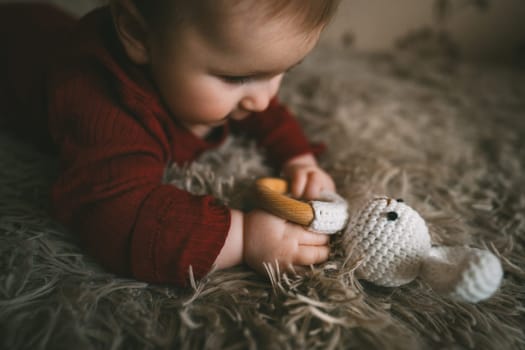 Adorable baby playing with bunny toy on fluffy brown bed coat. Babyhood and playtime concept. High quality photo