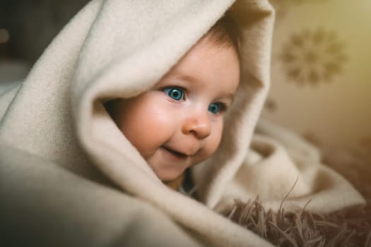 Smiling baby girl crawling on bed under the blanket. Adorable kid portrait. 5 month old child. Childhood concept. High quality photo