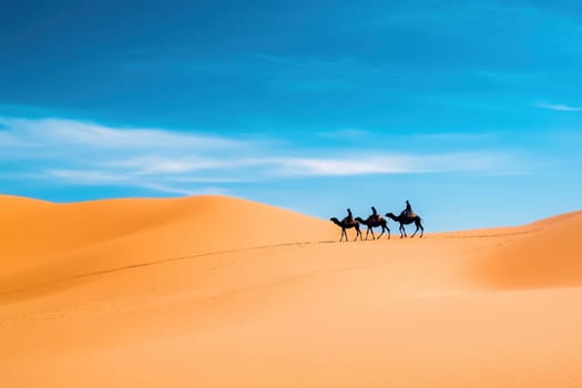 A group of people riding camels across a desert. The sky is blue and the sun is shining