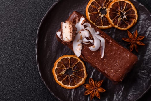 Piece of sweet chocolate bounty cake with coconut flakes and sponge cake on dark concrete background