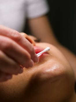 Moisturizing and nourishing lips in a beauty salon for a young Caucasian woman, close-up, vertical, stories