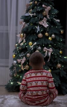 Christmas, a boy in New Year's pajamas sits on the floor and works on the Christmas tree. Rear view, without face