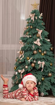 Christmas. A five-year-old boy in New Year's pajamas lies on the floor near the Christmas tree in a Santa Claus hat and smiles cheerfully. Facial expressions of joy and happiness. festive atmosphere