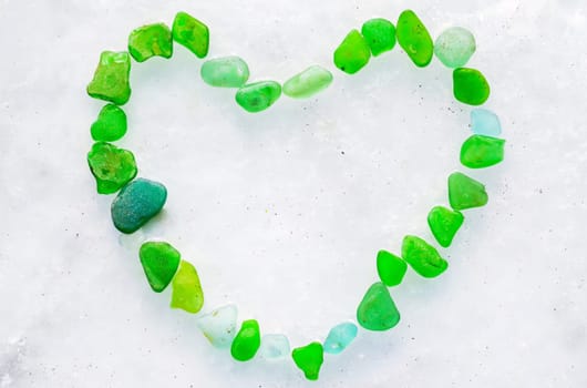 Heart made of green bottle glass on the ice of frozen Japanese sea. Glass beach, Russia.
