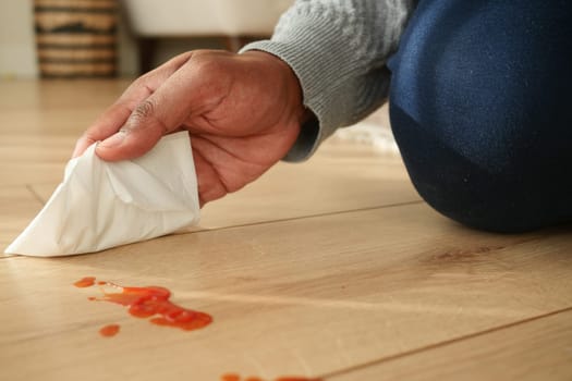 A person wipes a sauce spill on the floor.