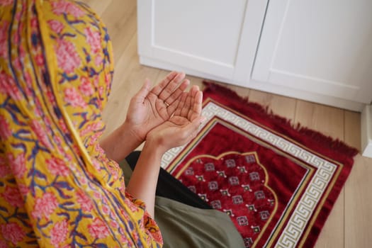 A woman kneels in prayer on a decorative rug indoors.