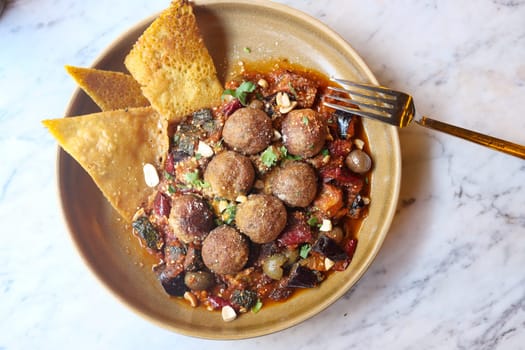 A bowl of meatballs in rich sauce garnished with herbs.