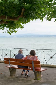 Meersburg, Germany - July 31, 2024: Older couple of pensionable age sitting on a bench on the shore of Lake Constance in Meersburg and enjoying the beautiful view