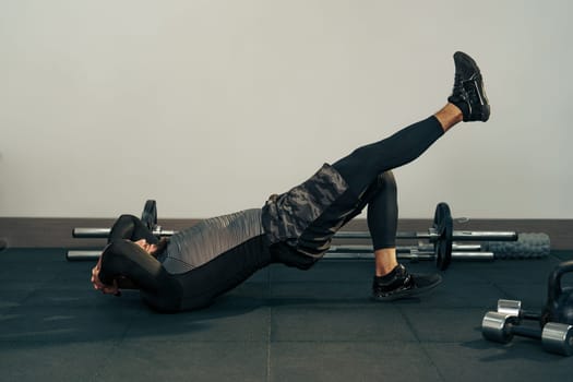 A person exercises on a gym mat, lifting one leg upward while keeping the other bent. This movement emphasizes core strength and is performed in a modern gym setting.