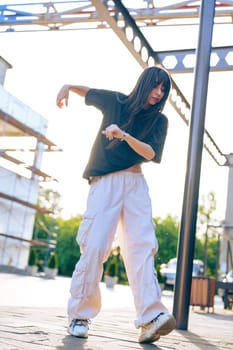 A dancer showcases dynamic movements wearing a loose black shirt and white cargo pants. The outdoor urban setting is bathed in golden light as the sun sets in the background.