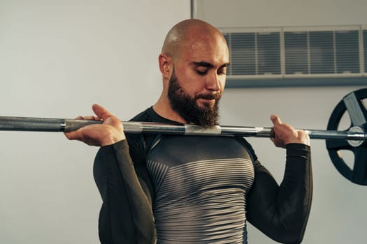A man with a beard is performing a bicep curl with a barbell in a gym. He is focused and wearing a fitted shirt, showcasing his athletic physique during an intense workout.