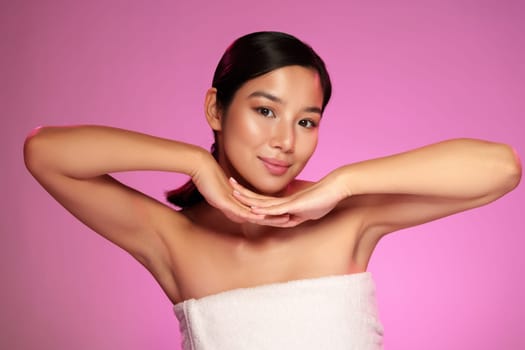 A young woman showcases a playful pose with her hands under her chin, smiling charmingly against a vibrant pink backdrop during a studio session.