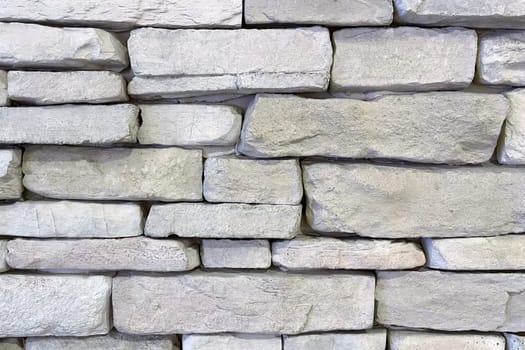 Textured Stone Wall Background.A close-up view of a textured stone wall. The wall is constructed from irregularly shaped, light-colored stones that are stacked in a horizontal pattern.