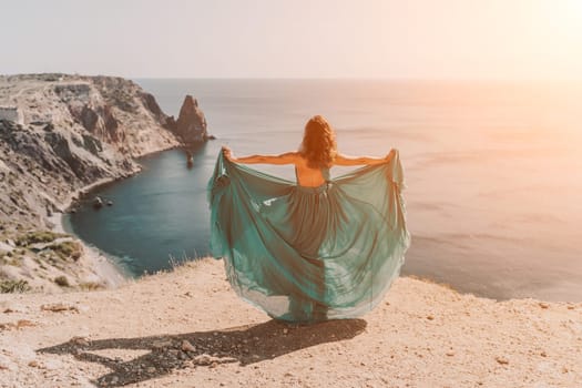 Woman green dress sea. Female dancer posing on a rocky outcrop high above the sea. Girl on the nature on blue sky background. Fashion photo