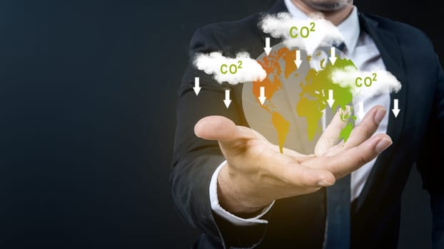 The business hand shows a virtual earth with a sign of carbon reduction for decreased CO2. Concepts of environmental protection, climate change, global warming, or net zero carbon neutral