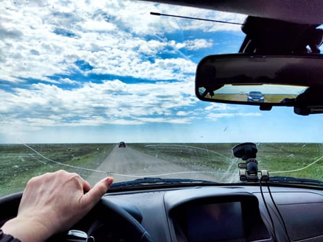 A driver navigates an open road with a cracked windshield while surrounded by green fields and a bright blue sky filled with clouds.