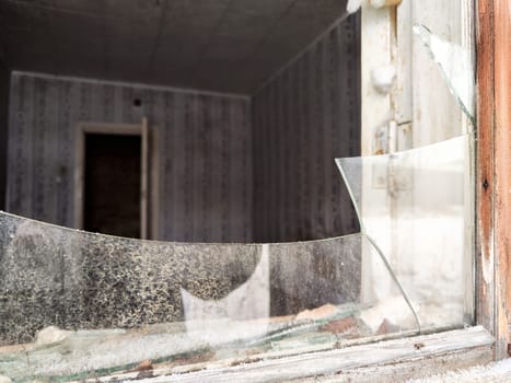 Shattered glass in a broken window showcases a neglected interior, suggesting abandonment and decay in a forlorn location.