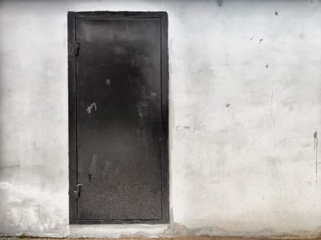 A black door stands prominently against a weathered gray wall, highlighting urban elements in broad daylight.