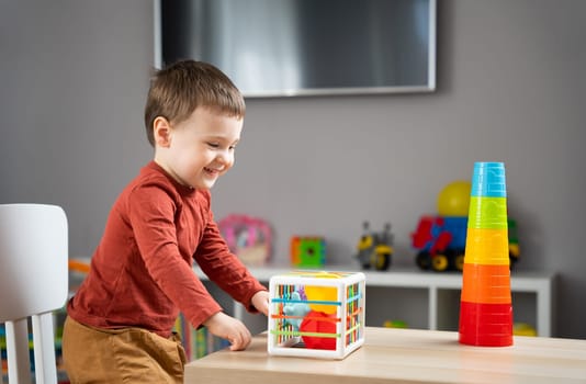 A cute little toddler boy of two years old plays with multi-colored balls and sits at a children's table in his room. Tactile sensory balls. Educational toys for children. Soft selective focus