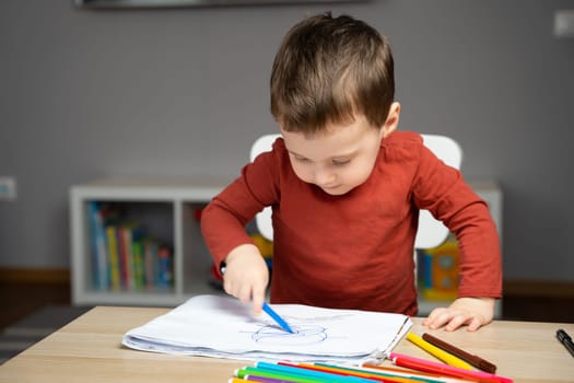 A cute little toddler boy of two years old draws with markers in the album in the children's room at home. Educational activities for kids