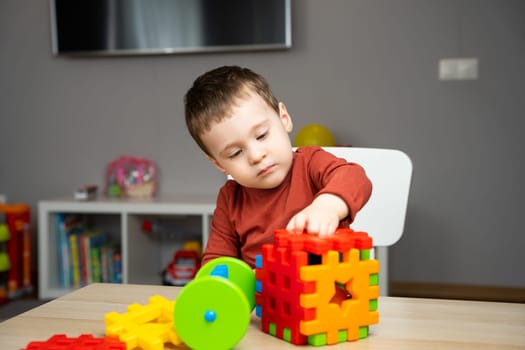 A cute attentive little toddler boy of two years old sits at a children's table and plays with multi-colored sorter. Educational logic toys for children. Soft selective focus