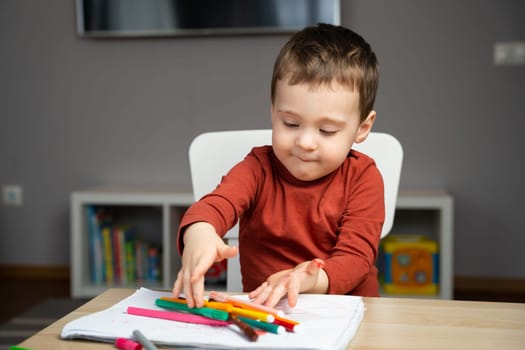A cute happy little toddler boy of two years playing with markers in the album in the children's room at home. Educational activities for kids. Selective focus.