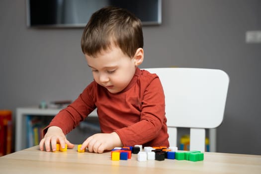 A cute little toddler boy of two years old sits at a children's table and plays with colorful cubes. Educational logic toys for children. Soft selective focus