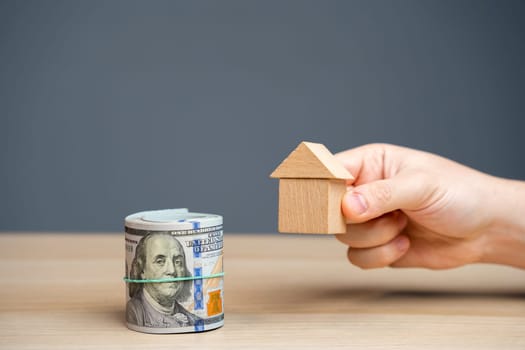 Wooden house in hands and money dollar bills. The concept of attracting investment in real estate. Mortgages and home loans. Buying and renting apartments. Taxation
