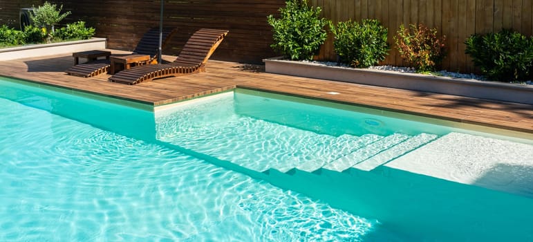 Modern swimming pool with turquoise water, wooden deck, and relaxing lounge chairs under sunny sky