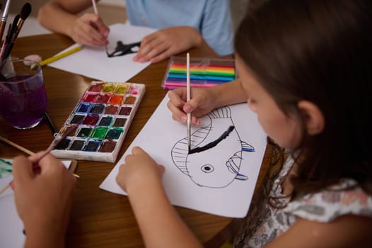 Young children engaged in a creative art activity, painting a vibrant fish with watercolor.