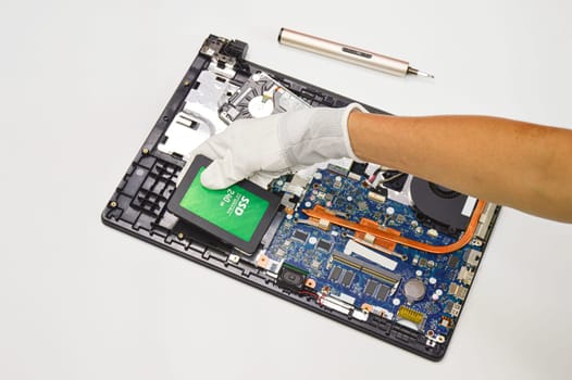 Photograph of a technician inserting a 240 GB ssd hard drive on a laptop motherboard on a white background.