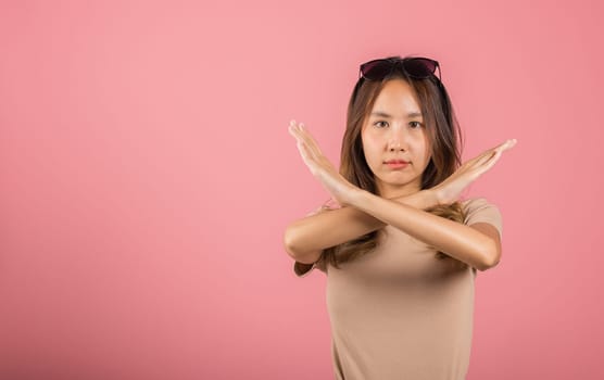 Portrait Asian beautiful young woman unhappy or confident standing holding two cross arms say no X stop sign, studio shot isolated pink background, Thai female pose reject gesture with copy space