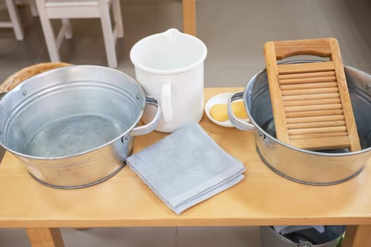 Montessori-style wash station featuring metal buckets, a wooden washboard, soap, and towels, designed for practical life skill activities.