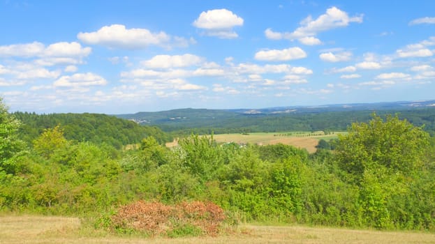 Vast landscape with green forests, rolling hills and a blue sky with white clouds. Idyllic nature, peace and freedom in a summery setting.