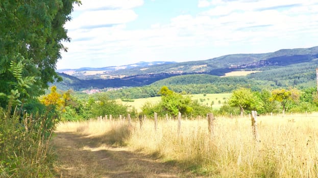 Vast landscape with green forests, rolling hills and a blue sky with white clouds. Idyllic nature, peace and freedom in a summery setting.