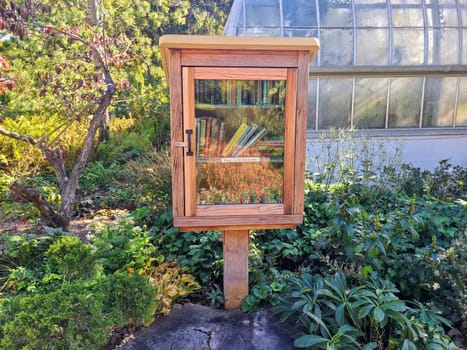 Charming free library nestled in a lush garden invites community sharing and reading in Cincinnati Ohio. Surrounded by vibrant greenery and a greenhouse backdrop, it is a serene escape for book lovers.