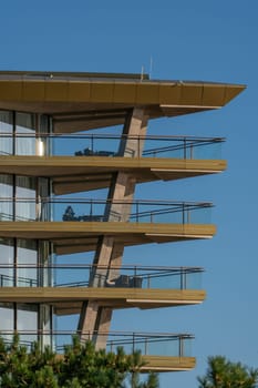 A close-up of a modern building with multiple balconies. The building has a unique angled design and is made of wood and glass.