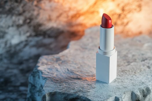 A red lipstick is sitting on a rock. The lipstick is white and the rock is grey. The image has a moody and mysterious feel to it
