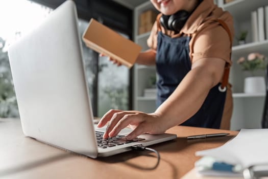 An e-commerce entrepreneur multitasking at her home office, typing on her laptop while handling a shipment, demonstrating her commitment to her online business.