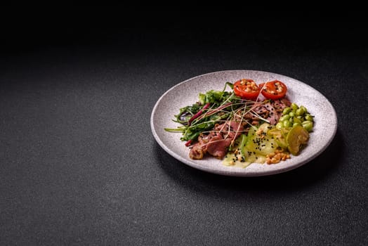 Warm salad consisting of slices of roast beef, greens, tomatoes, cucumbers, green beans on a dark concrete background