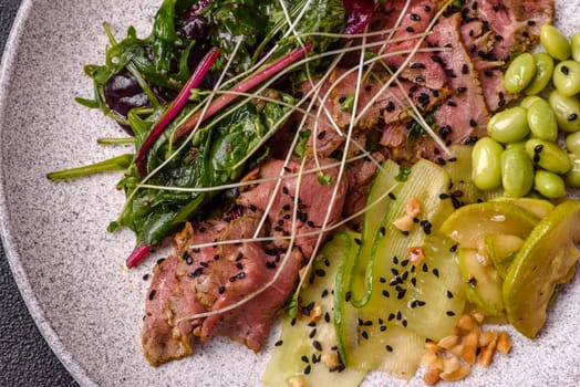 Warm salad consisting of slices of roast beef, greens, tomatoes, cucumbers, green beans on a dark concrete background