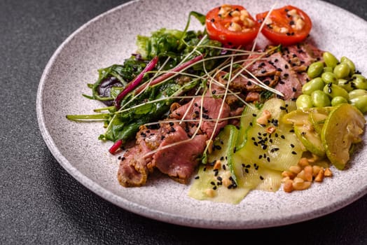 Warm salad consisting of slices of roast beef, greens, tomatoes, cucumbers, green beans on a dark concrete background