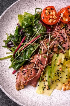 Warm salad consisting of slices of roast beef, greens, tomatoes, cucumbers, green beans on a dark concrete background