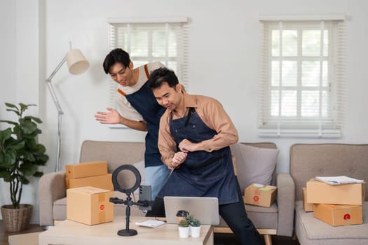 Two young Asian entrepreneurs excitedly filming an unboxing video in their home office, showcasing their products and engaging with their audience.