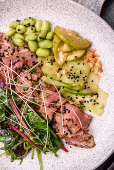 Warm salad consisting of slices of roast beef, greens, tomatoes, cucumbers, green beans on a dark concrete background
