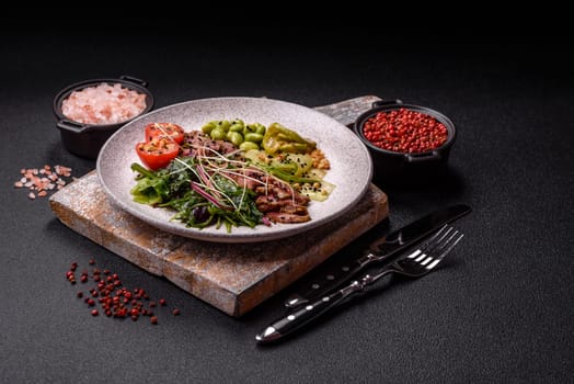 Warm salad consisting of slices of roast beef, greens, tomatoes, cucumbers, green beans on a dark concrete background